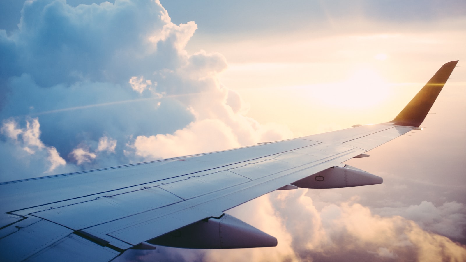 A wing view from an airplane window over clouds at golden hour, mid-flight