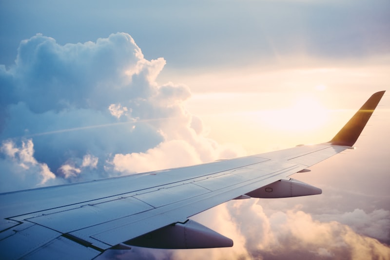 A wing view from an airplane window over clouds at golden hour, mid-flight