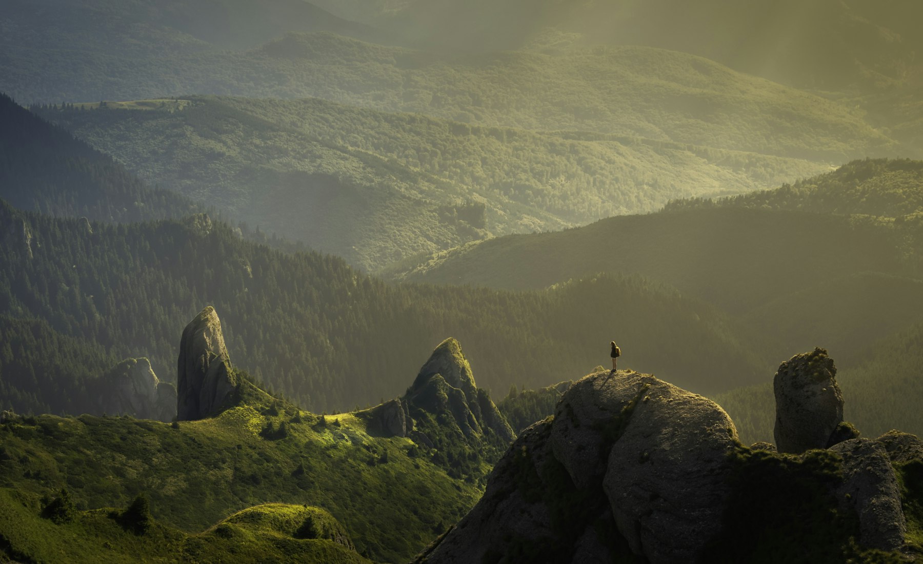 A traveller looking out over a vast mountain landscape at dawn